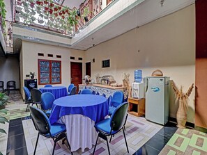 A dining area with round tables covered in blue tablecloths, chairs, a water dispenser, a refrigerator, and a decorative vase. - Oyo 91480 Putridapisa Syariah (Bangil)