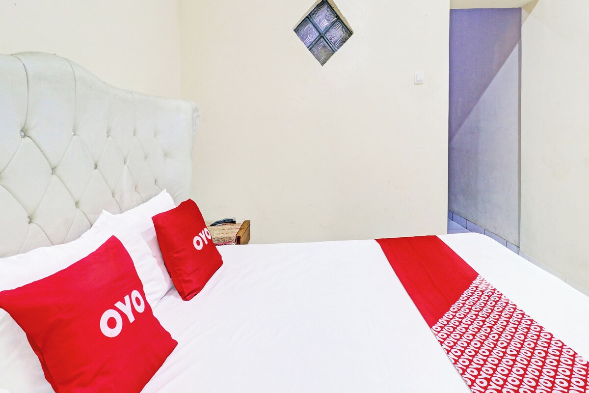 A bed with white and red bedding, a tufted headboard, a small window, and a door.