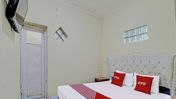 A hotel room with a bed, a small table, a window, and a door. - Oyo 91480 Putridapisa Syariah (Bangil)