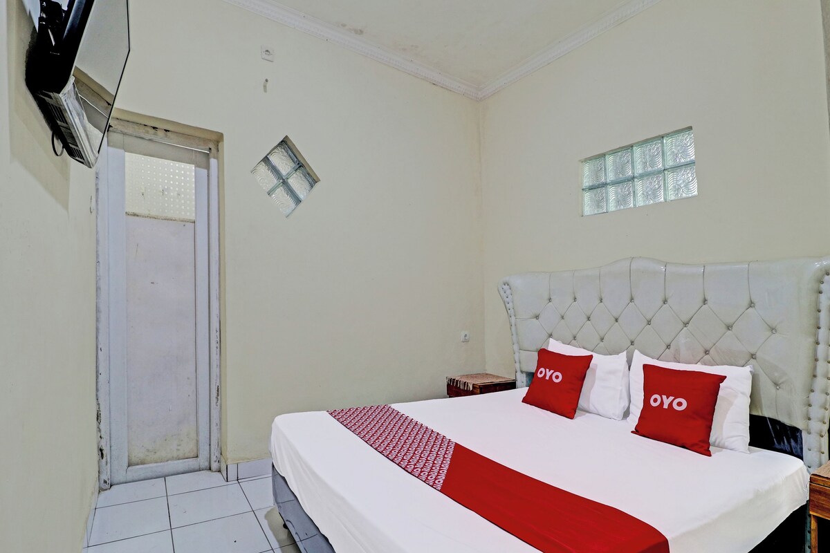 A hotel room with a bed, a small table, a window, and a door.