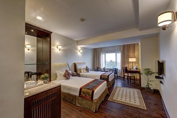 A hotel room with two beds, a desk, a chair, a TV, and a large window. - The Fern Residency Asansol (Asansol)