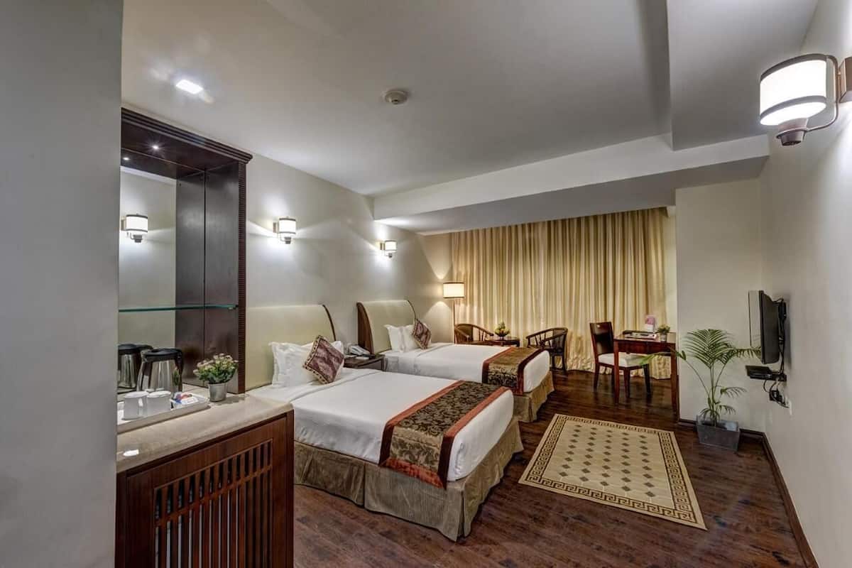 Habitación de hotel con dos camas, un escritorio, una silla, un televisor y un espejo.