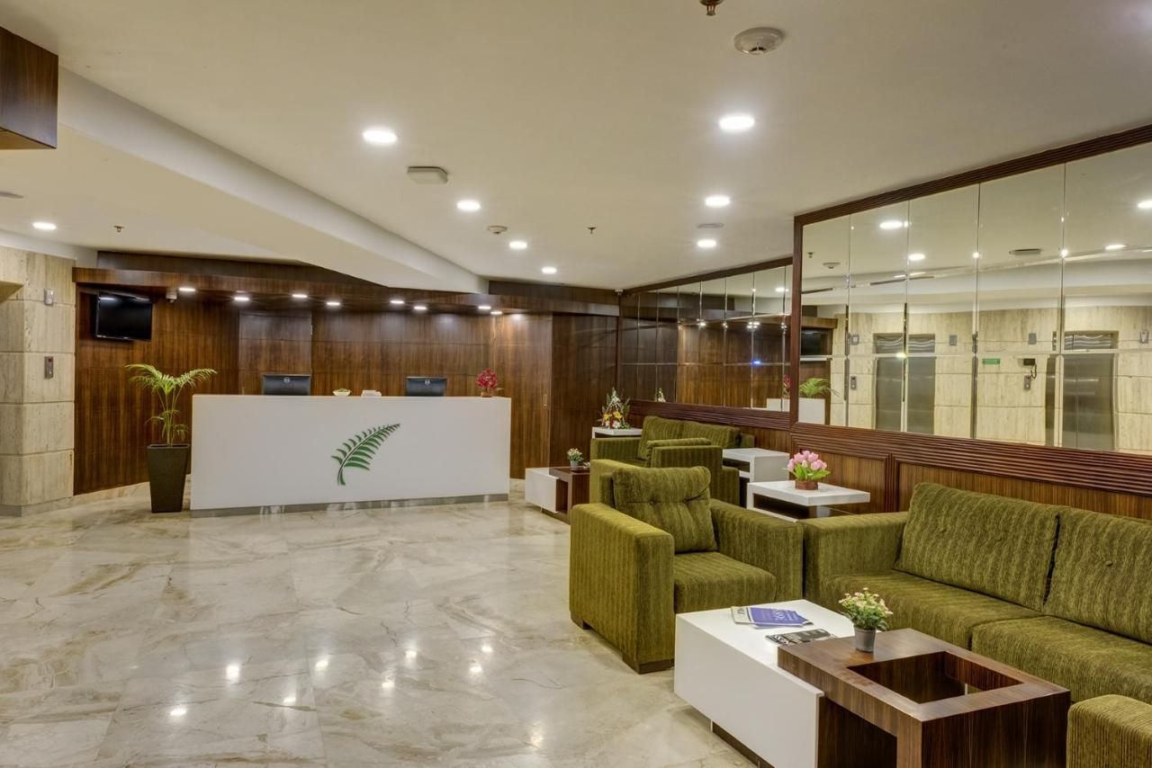 Un vestíbulo con mostrador de recepción, asientos tapizados en verde, una mesa de centro blanca y un espejo grande.