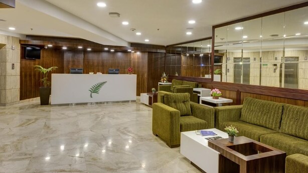 A lobby with a reception desk, green upholstered seating, a white coffee table, and a large mirror. - The Fern Residency Asansol (Asansol)