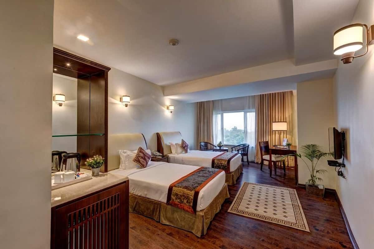 Una habitación de hotel con dos camas, un escritorio, una silla, un televisor y un ventanal grande.