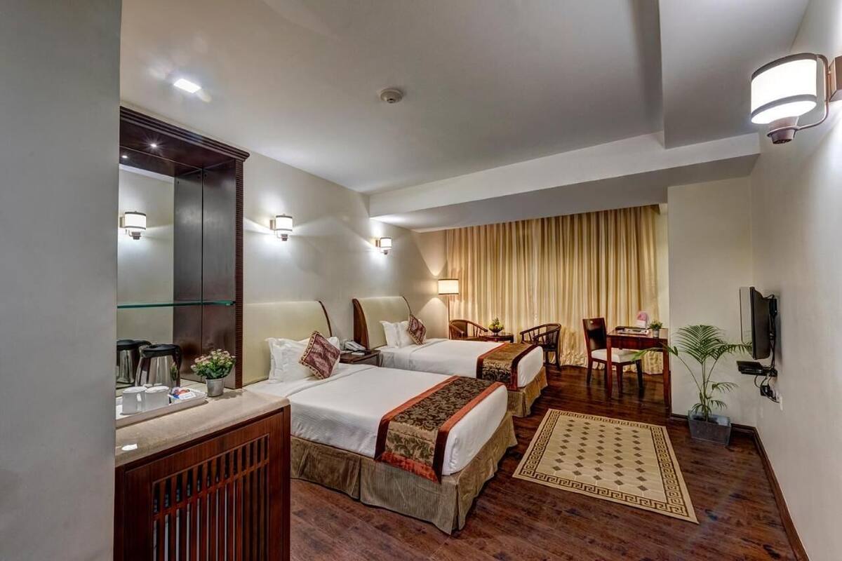 Habitación de hotel con dos camas, un escritorio, una silla, un televisor y un espejo.