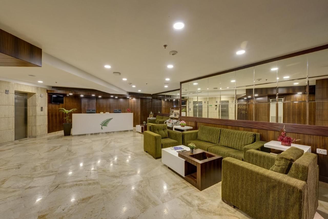 A lobby with a reception desk, green sofas, a white coffee table, and a marble floor.