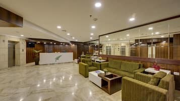 Un hall con mostrador de recepción, sofás verdes, una mesa de centro blanca y suelo de mármol.