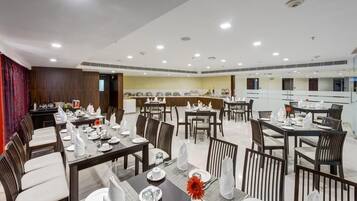 A hotel dining area with multiple tables set for service, a kitchen in the background, and a modern interior design.