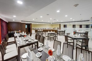 A hotel dining area with multiple tables set for service, a kitchen in the background, and a modern interior design. - The Fern Residency Asansol (Asansol)