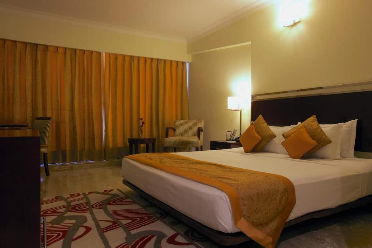 Una habitación de hotel con una cama grande, un escritorio, una silla, una lámpara y cortinas.
