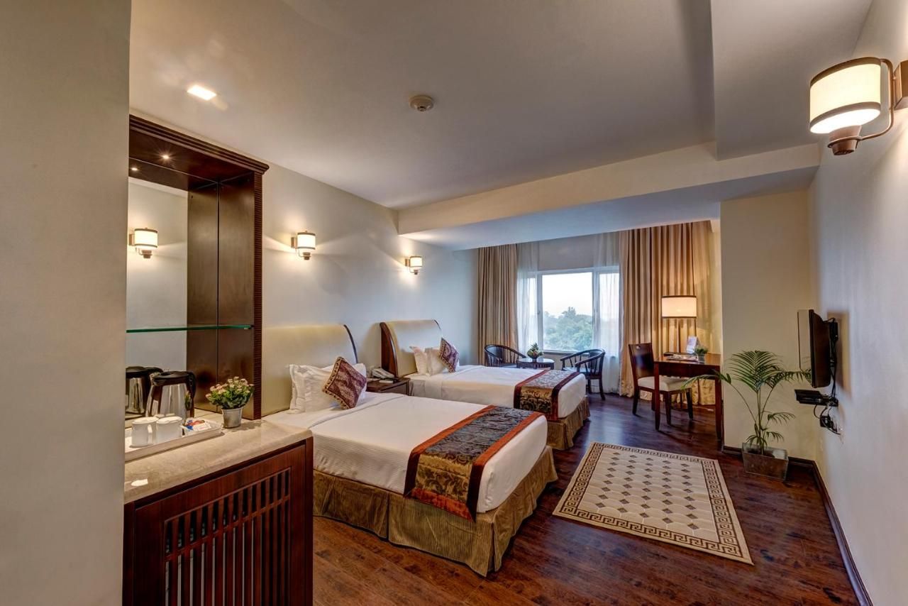 A hotel room with two beds, a desk, a chair, a TV, and a large window.