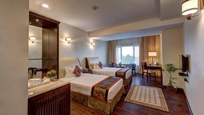 A hotel room with two beds, a desk, a chair, a TV, and a large window. - The Fern Residency Asansol (Asansol)