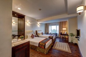 A hotel room with two beds, a desk, a chair, a television, and a window with curtains. - The Fern Residency Asansol (Asansol)