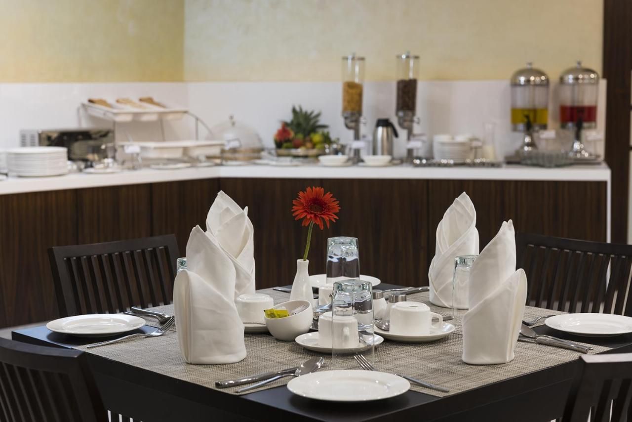 A breakfast buffet setup with a variety of food items, a vase with a red flower, and neatly arranged dining ware.