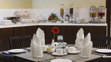 A breakfast buffet setup with a variety of food items, a vase with a red flower, and neatly arranged dining ware.