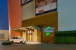 A hotel entrance with a covered driveway, a neon sign, and a parked car.