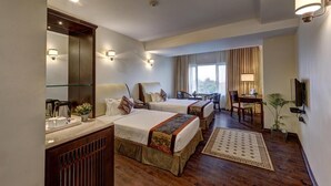 A hotel room with two beds, a desk, a chair, a TV, and a large window. - The Fern Residency Asansol (Asansol)