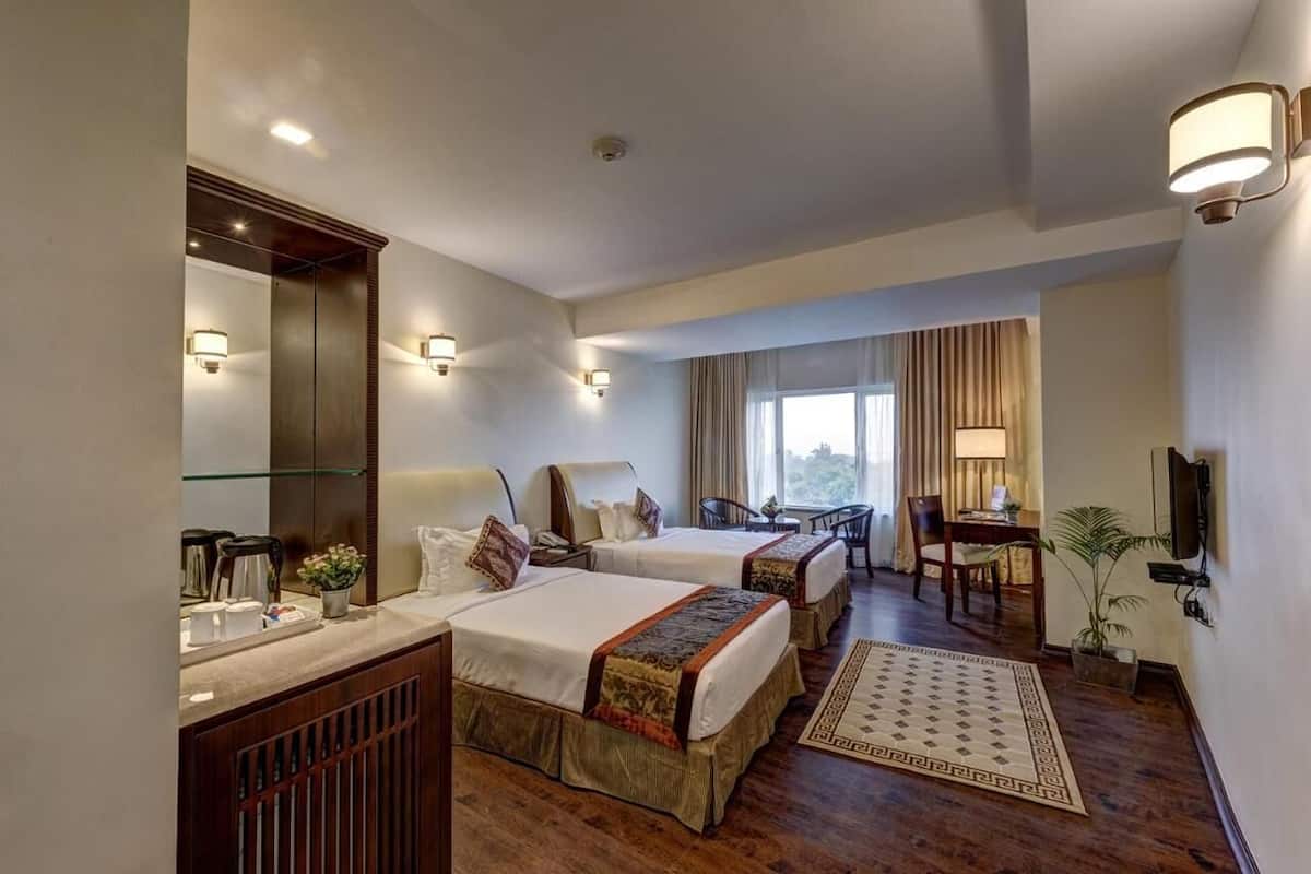 Habitación de hotel con dos camas, un escritorio, una silla, un televisor y un ventanal grande.
