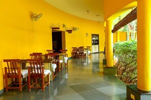 A dining area with yellow walls, wooden chairs, and tables. - Sterling Arunai Anantha Tiruvannamalai (Tiruvannamalai)
