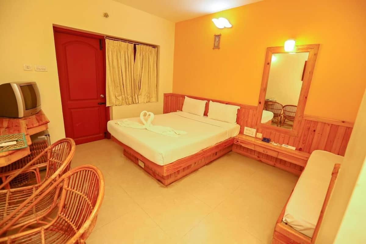 A room with a bed, a television, a desk, and wicker chairs.