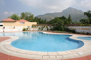 A swimming pool with a curved design, surrounded by a tiled deck. - Sterling Arunai Anantha Tiruvannamalai (Tiruvannamalai)