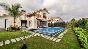 Een modern huis met een zwembad, een terras met zitplaatsen en een verzorgd gazon.