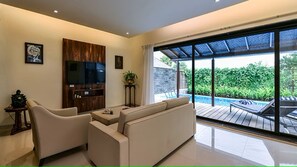 A modern living room with a sofa, a television, and a large window overlooking a pool. - U Tropicana Resort & Spa (Alibag)