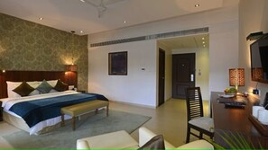 A hotel room with a bed, a desk, a chair, and a television. - U Tropicana Resort & Spa (Alibag)