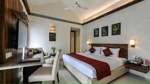 A hotel room with a bed, desk, chair, TV, artwork, and bedside lamps. - U Tropicana Resort & Spa (Alibag)
