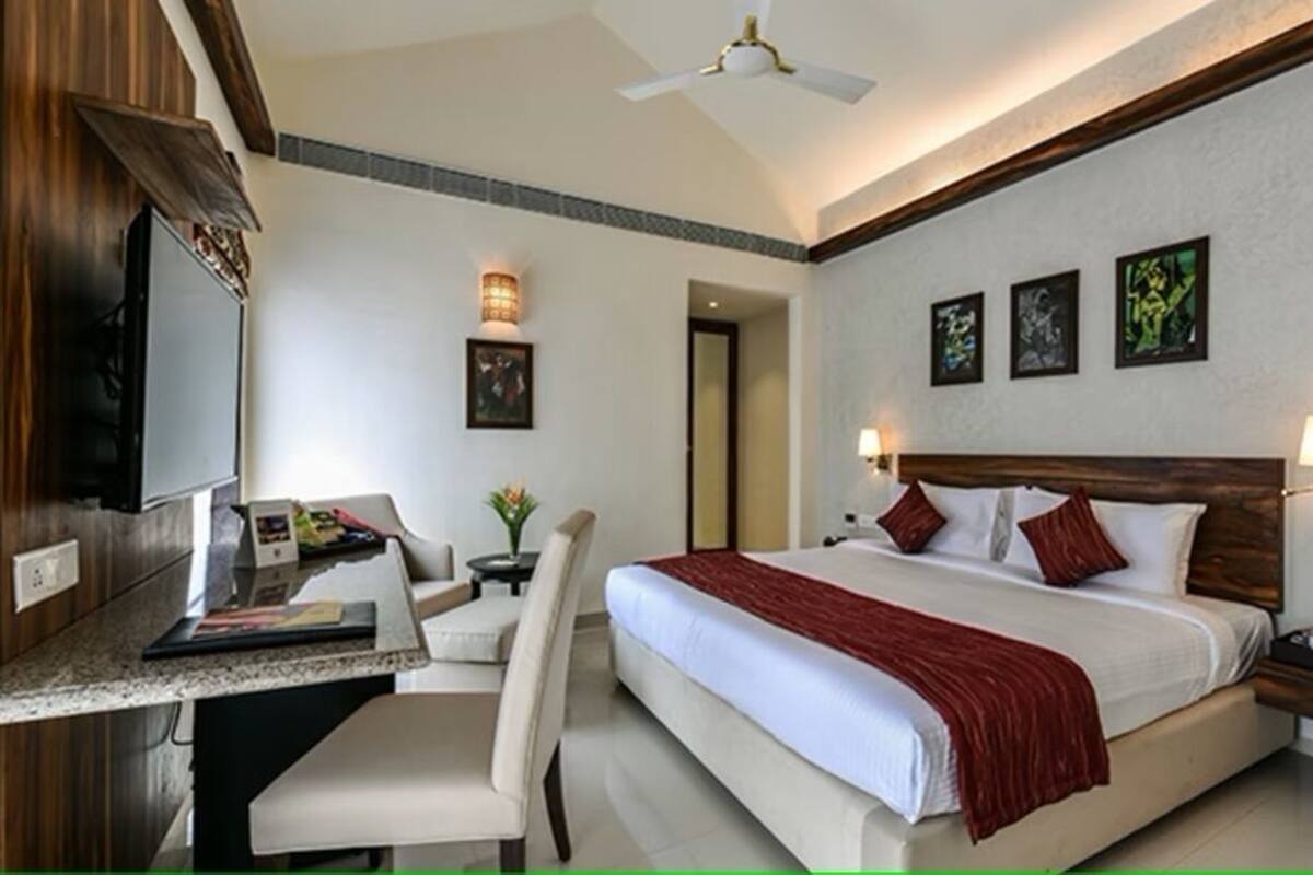 A hotel room with a bed, desk, chair, TV, artwork, and bedside lamps.