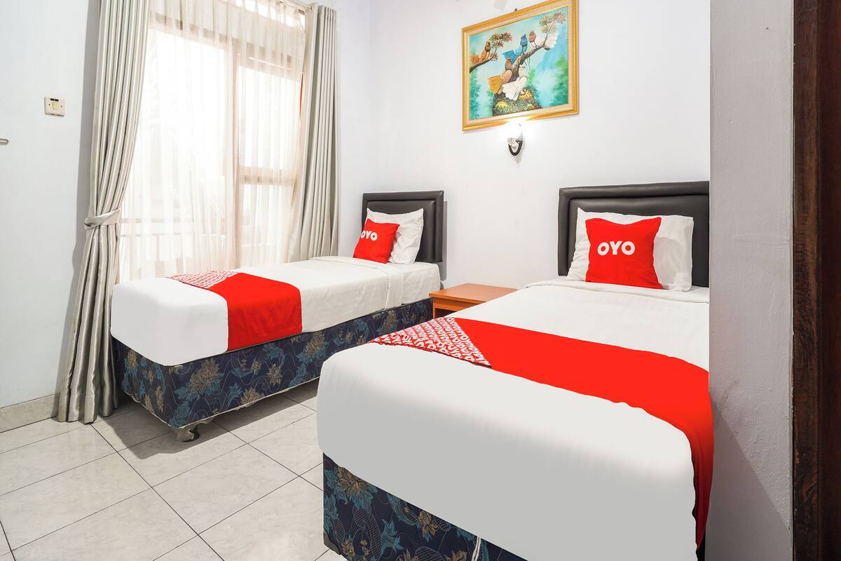 Habitación de hotel con dos camas, cada una con una colcha roja y blanca, un cuadro en la pared y un equipo de aire acondicionado.