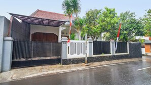 A residential area with a gated entrance, a house with a tiled roof, and a palm tree. - Oyo 91561 Gandhi Hotel (Bandung)
