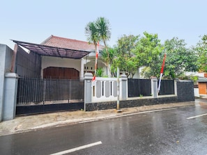 A residential area with a gated entrance, a house with a tiled roof, and a palm tree. - Oyo 91561 Gandhi Hotel (Bandung)