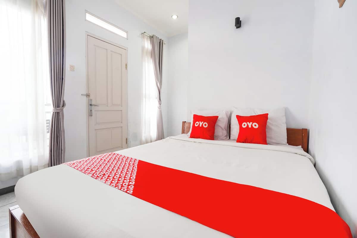 Una habitación de hotel con una cama, paredes blancas, una puerta y cortinas.