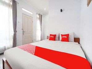 Et hotelværelse med seng, hvide vægge, en dør og gardiner.