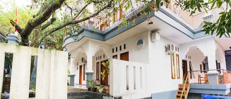 A building with a staircase leading to a balcony, a blue car parked nearby, and a tree with green leaves.