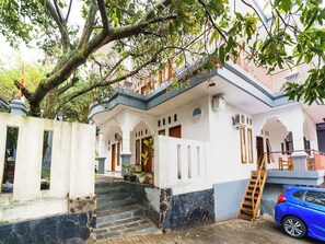 Un bâtiment avec un escalier menant à un balcon, une voiture bleue garée à proximité et un arbre aux feuilles vertes.