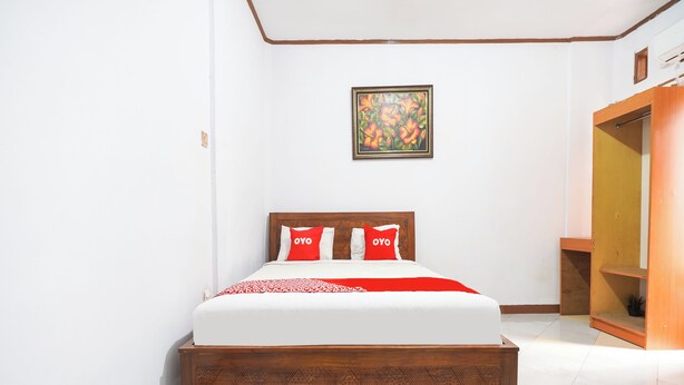 A neatly made bed with a wooden headboard, a red and white bedspread, and two red pillows with 'OYO' on them. - Oyo 91561 Gandhi Hotel (Bandung)