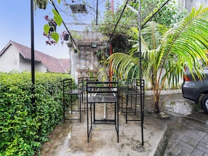 A garden with metal furniture, a car, and a building in the background. - Oyo 91561 Gandhi Hotel (Bandung)