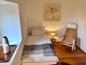 Un dormitorio con una cama, una silla, una lámpara y una obra de arte en la pared.