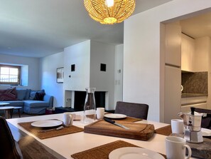 Una sala de estar moderna con comedor, chimenea y cocina visible a través de un vano abierto.