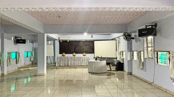 A spacious room with a tiled floor, a projector screen, a ceiling fan, and a table with a white tablecloth.