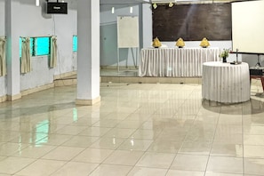 Ein geräumiger Saal mit Fliesenboden, einem weißen Tisch mit einer Vase und einer Projektionsleinwand.