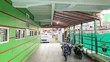 A covered parking area with a green wall, a tiled floor, and a metal roof.
