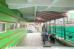 Un área de estacionamiento techada con un muro verde, piso de baldosas y techo metálico.