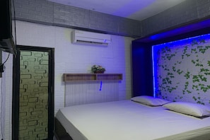 A bedroom with a bed, an air conditioning unit, a wall-mounted shelf with a plant, and a decorative wall with leaf patterns. - Oyo 91757 Surya Hotel (Watansoppeng)