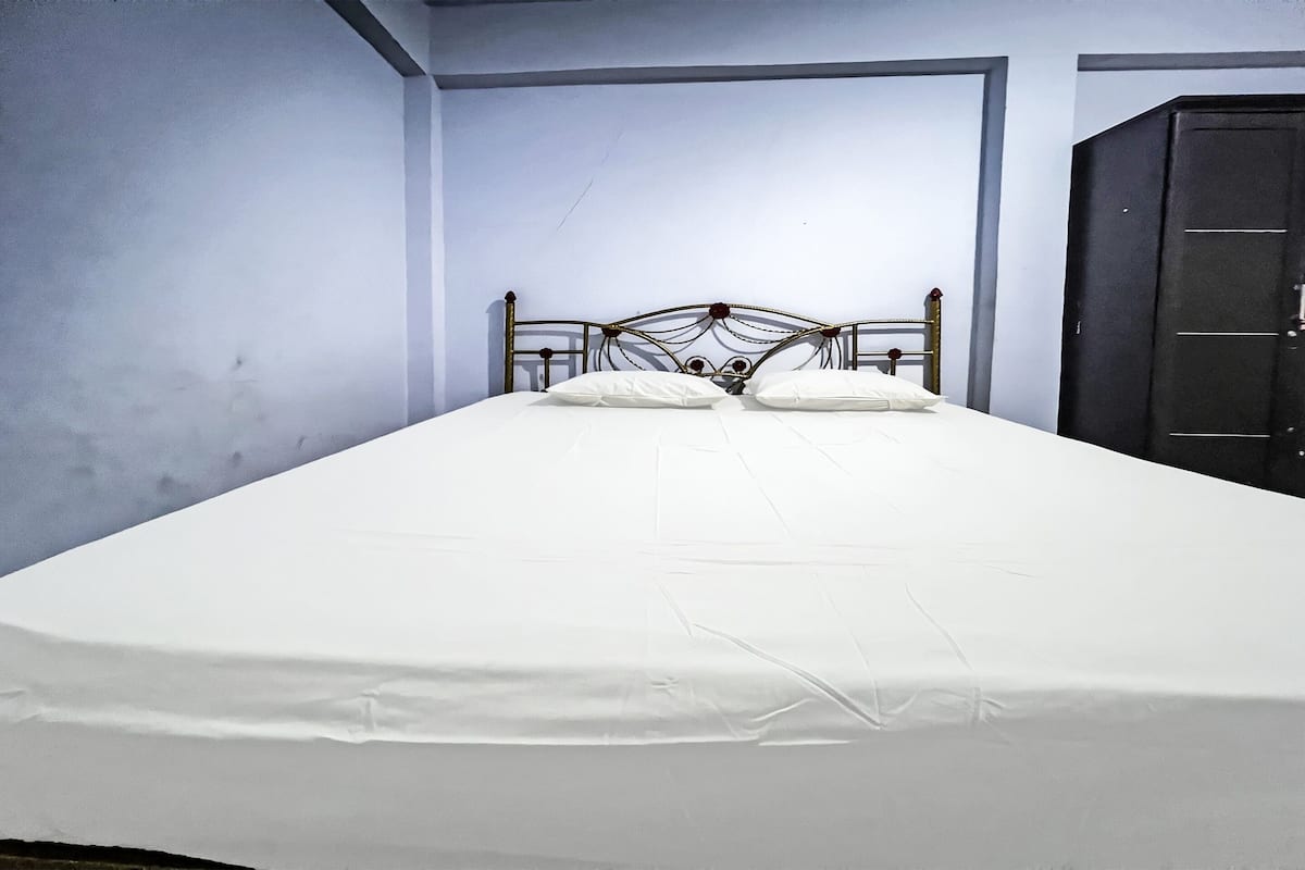 A single bed with a metal headboard in a room with plain walls and a dark wardrobe.