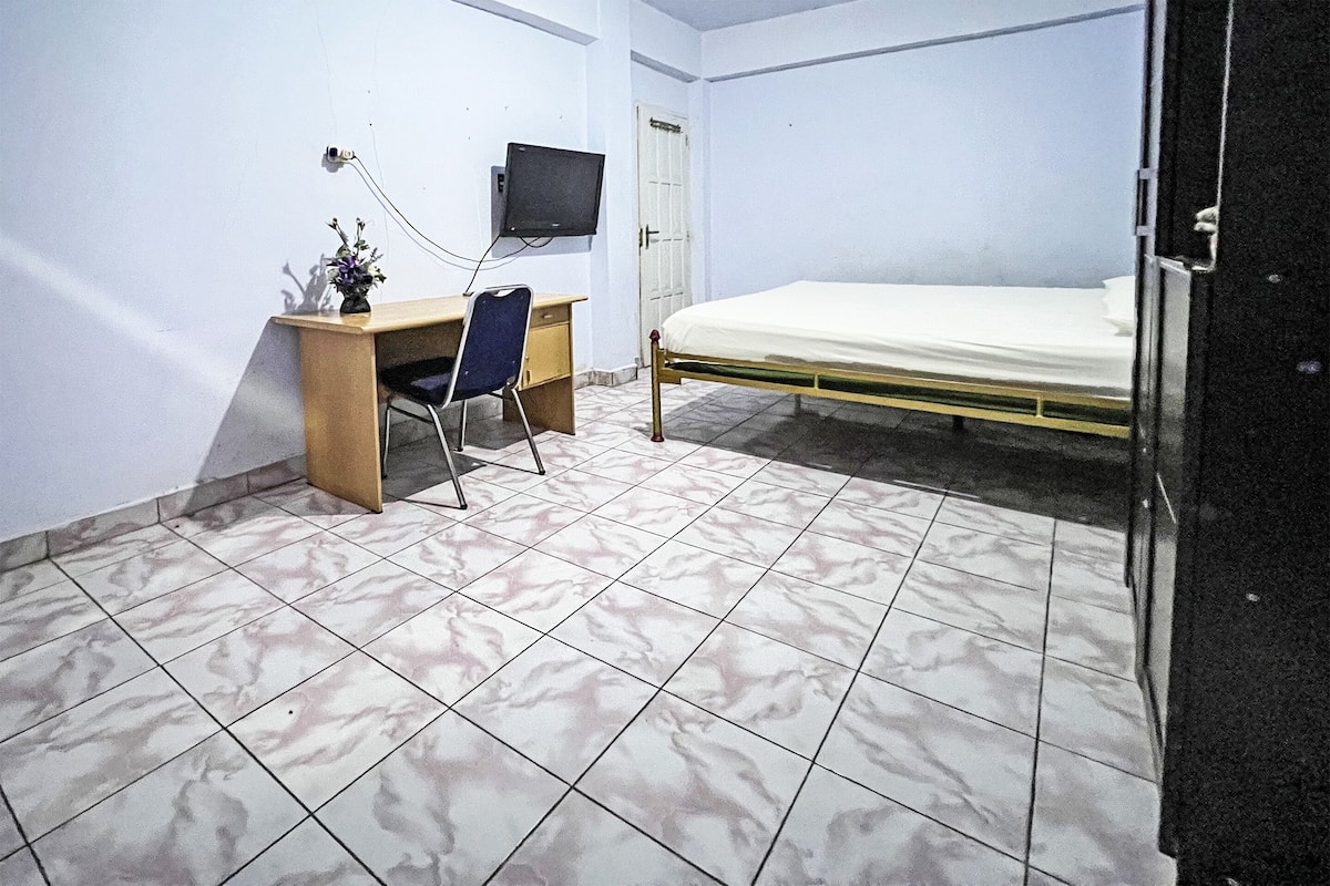 A bedroom with a bed, a desk with a chair, a television, and a door.