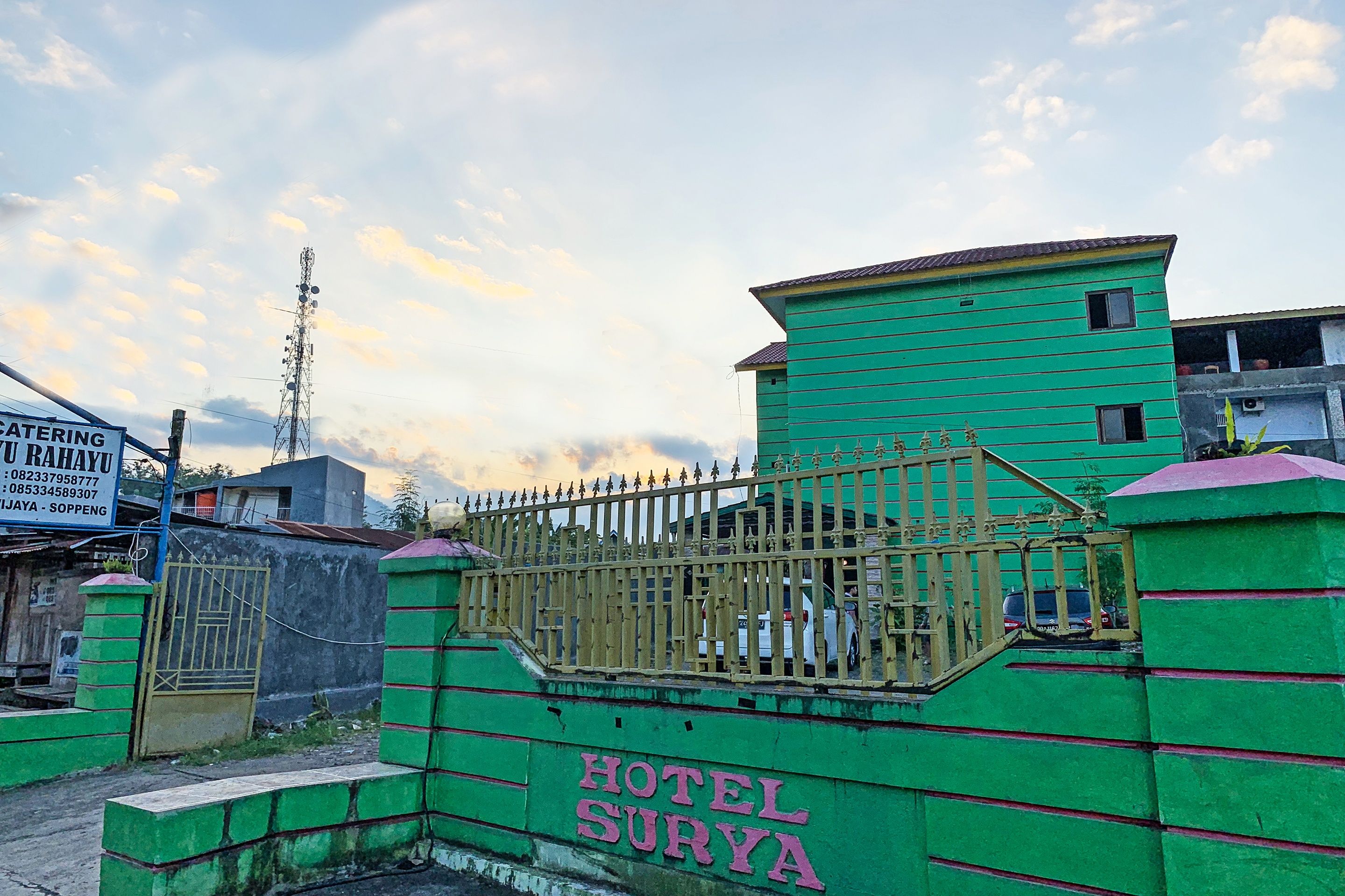 Un bâtiment vert, sur lequel on peut lire l’inscription « HÔTEL SURYA », et une entrée fermée par un portail.